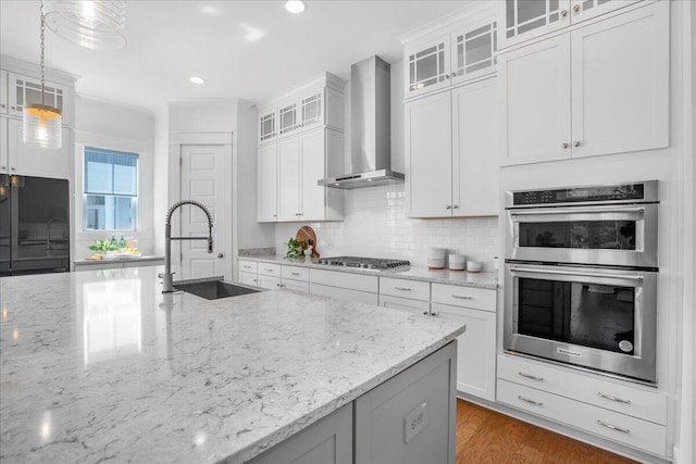 kitchen featuring a sink, appliances with stainless steel finishes, wall chimney exhaust hood, backsplash, and white cabinetry
