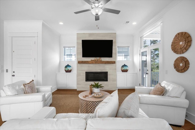 living room featuring ceiling fan, a fireplace, wood-type flooring, and ornamental molding