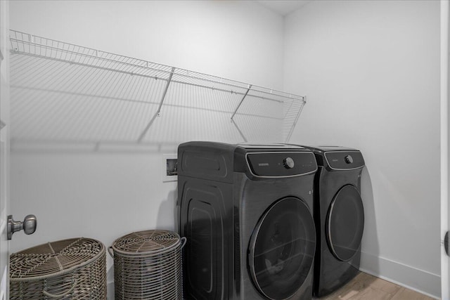 clothes washing area with washing machine and dryer and light hardwood / wood-style flooring