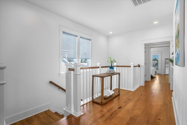 hallway with an upstairs landing, wood finished floors, and recessed lighting
