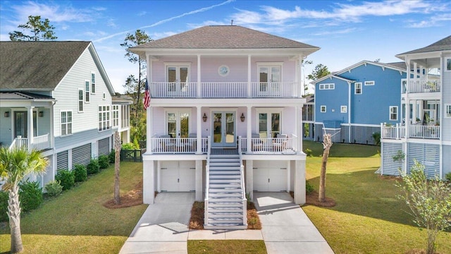 raised beach house with french doors, stairway, concrete driveway, a garage, and a front lawn