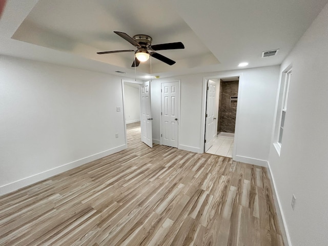 unfurnished bedroom featuring ensuite bathroom, a tray ceiling, ceiling fan, and light hardwood / wood-style flooring