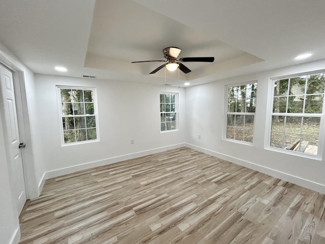 spare room featuring ceiling fan, plenty of natural light, light wood-type flooring, and a tray ceiling