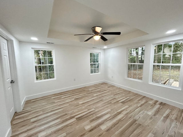 unfurnished room with a raised ceiling, ceiling fan, a wealth of natural light, and light wood-type flooring