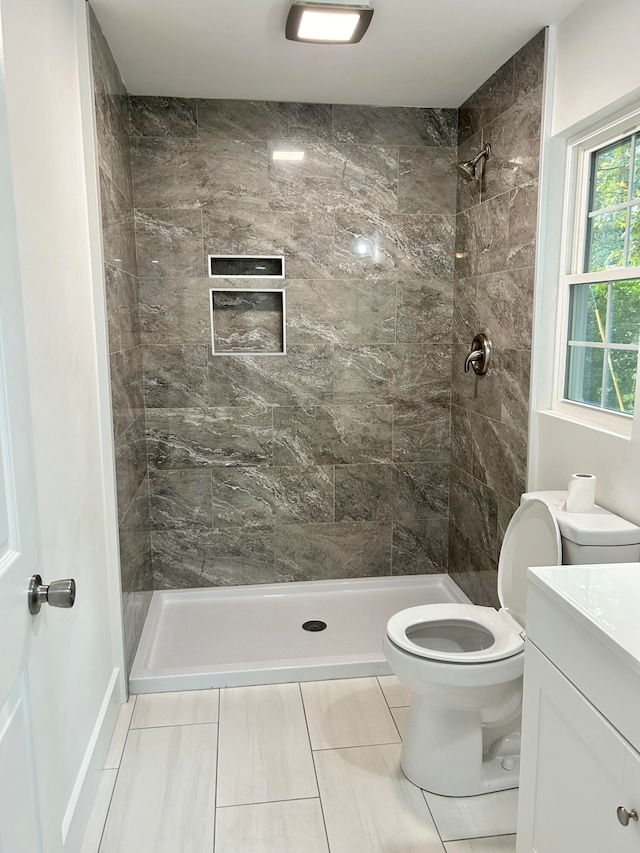 bathroom featuring tile patterned flooring, vanity, a tile shower, and toilet