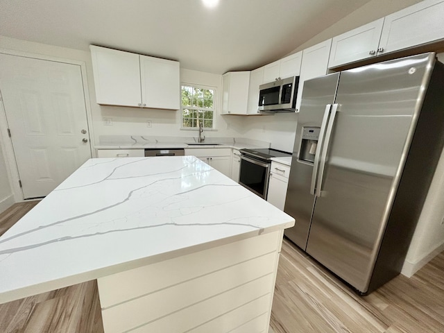 kitchen with sink, white cabinetry, a kitchen island, stainless steel appliances, and light stone countertops