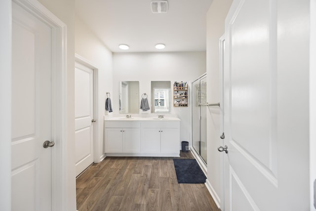 bathroom with a sink, wood finished floors, visible vents, a shower stall, and double vanity