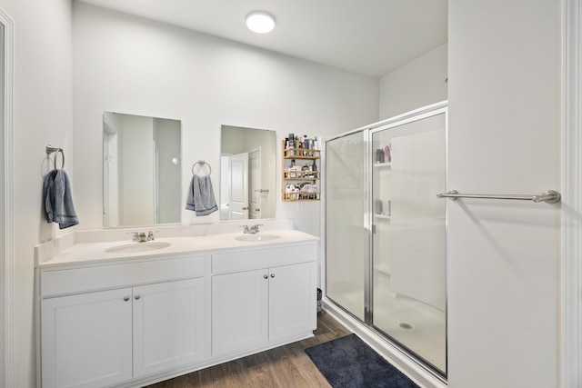 bathroom with double vanity, wood finished floors, a stall shower, and a sink