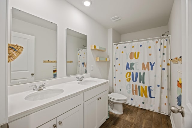 full bath featuring toilet, double vanity, a sink, and wood finished floors