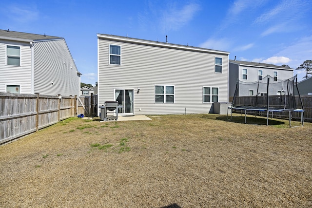 rear view of property featuring a patio area, a fenced backyard, a trampoline, and a yard