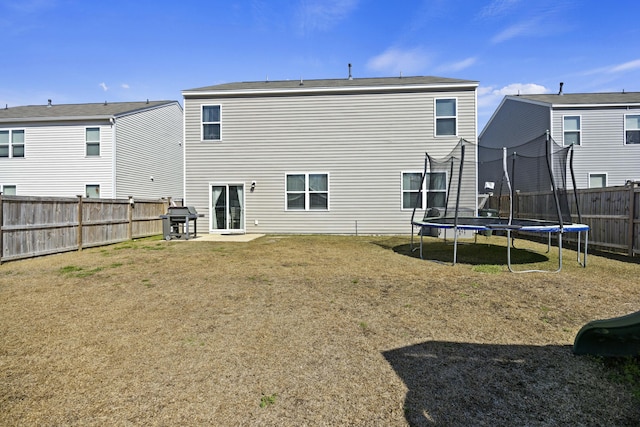 rear view of property with a trampoline, a fenced backyard, and a yard