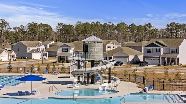 community pool with a residential view, a water slide, fence, and a patio