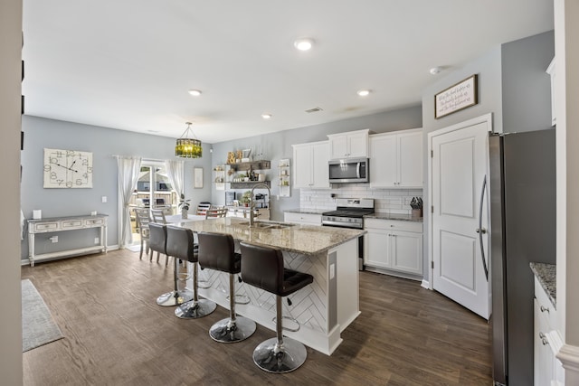 kitchen with white cabinets, appliances with stainless steel finishes, light stone counters, a sink, and backsplash