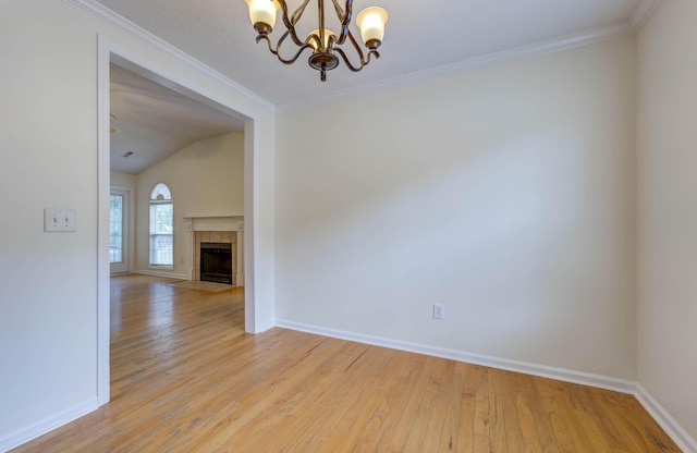 empty room featuring baseboards, a notable chandelier, a tiled fireplace, and light wood finished floors