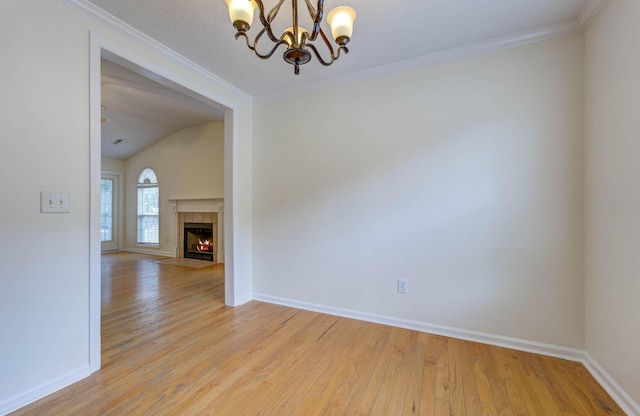 spare room featuring an inviting chandelier, light wood finished floors, a tiled fireplace, baseboards, and ornamental molding