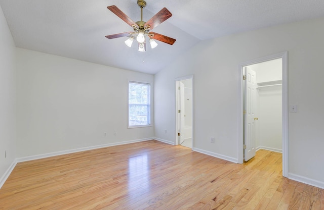unfurnished bedroom with baseboards, light wood finished floors, a walk in closet, and lofted ceiling