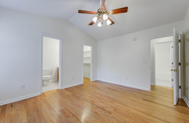 unfurnished bedroom featuring lofted ceiling, baseboards, ensuite bathroom, a walk in closet, and light wood finished floors