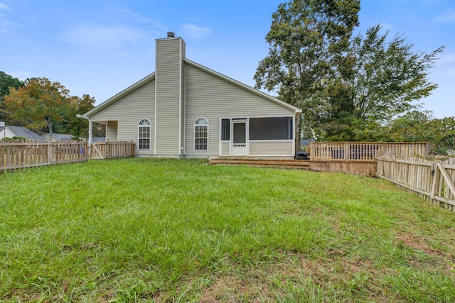 back of house featuring a lawn, a chimney, a fenced backyard, and a sunroom