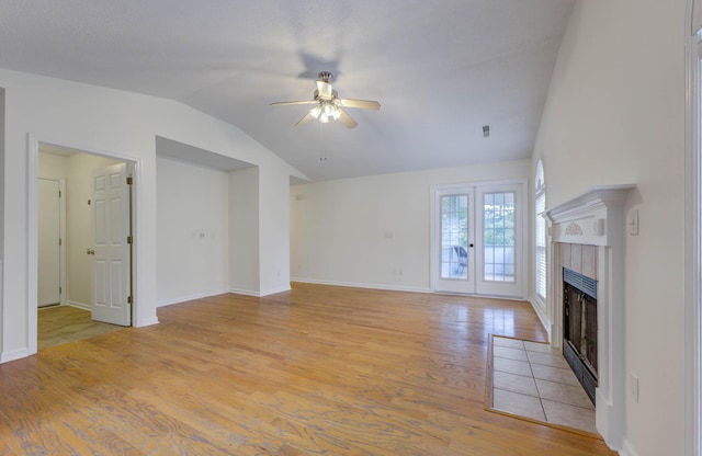 unfurnished living room with a ceiling fan, a tile fireplace, baseboards, lofted ceiling, and light wood-style flooring