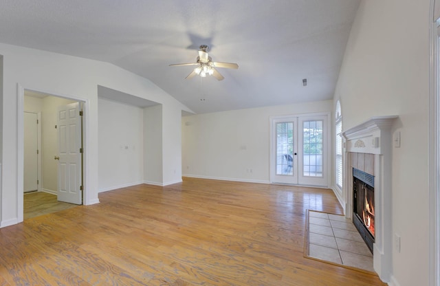 unfurnished living room with ceiling fan, light wood finished floors, a fireplace, baseboards, and vaulted ceiling