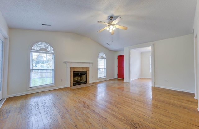 unfurnished living room featuring ceiling fan, light wood-style floors, a tiled fireplace, vaulted ceiling, and visible vents