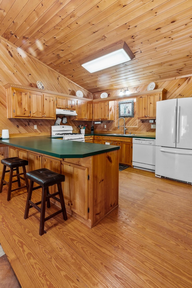 kitchen with light wood-style flooring, under cabinet range hood, a peninsula, white appliances, and dark countertops