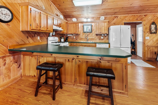 kitchen featuring white appliances, lofted ceiling, a peninsula, wood walls, and a sink