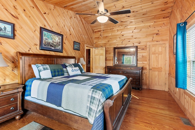 bedroom featuring visible vents, ceiling fan, wood finished floors, a high ceiling, and wood walls