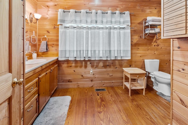 bathroom with toilet, wooden walls, wood finished floors, vanity, and visible vents