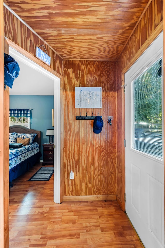 corridor featuring wooden walls, wooden ceiling, and light wood-style flooring