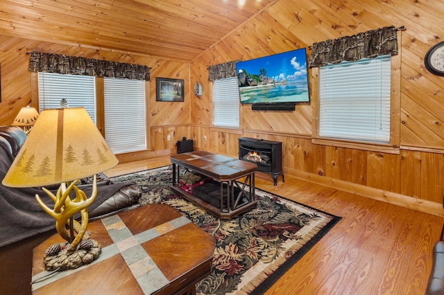 living area with wooden walls, lofted ceiling, wood ceiling, wood finished floors, and a wood stove