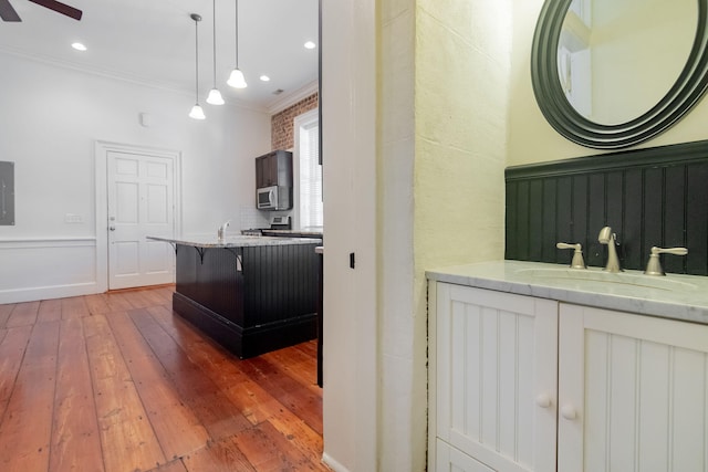 interior space featuring a breakfast bar area, crown molding, ceiling fan, wood-type flooring, and sink