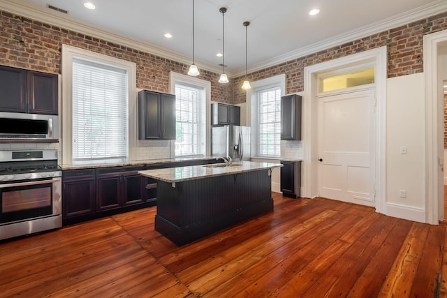 kitchen featuring decorative light fixtures, hardwood / wood-style flooring, light stone countertops, a center island with sink, and appliances with stainless steel finishes