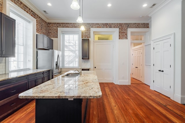 kitchen with pendant lighting, stainless steel fridge with ice dispenser, brick wall, sink, and light stone counters