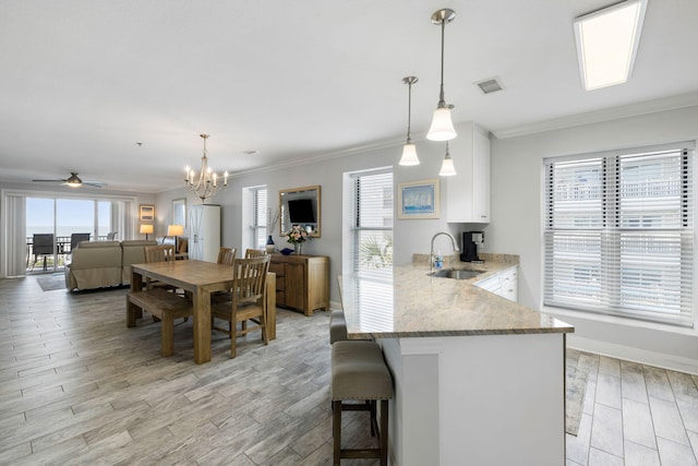 kitchen featuring ornamental molding, white cabinetry, light stone counters, a sink, and light wood-style flooring