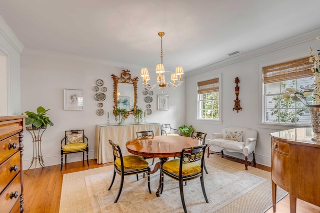 dining area with light hardwood / wood-style floors, ornamental molding, and a notable chandelier