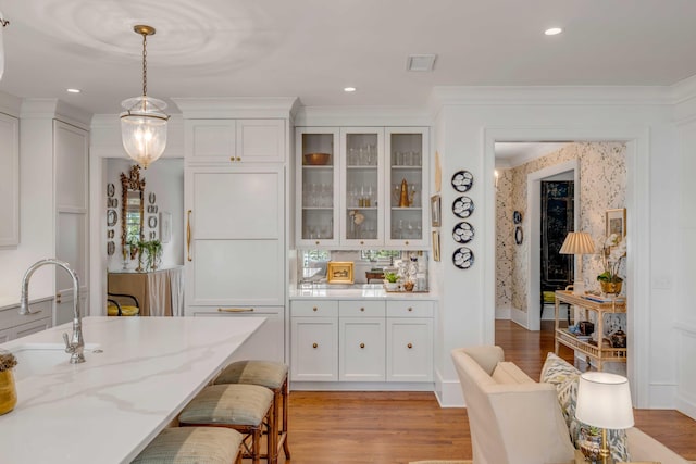 kitchen featuring light hardwood / wood-style flooring, light stone counters, white cabinetry, and decorative light fixtures