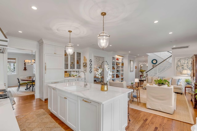 kitchen with white cabinetry, a center island with sink, light hardwood / wood-style floors, and sink