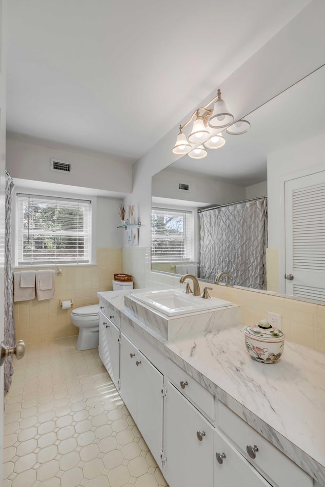 bathroom with tile walls, vanity, toilet, and a wealth of natural light