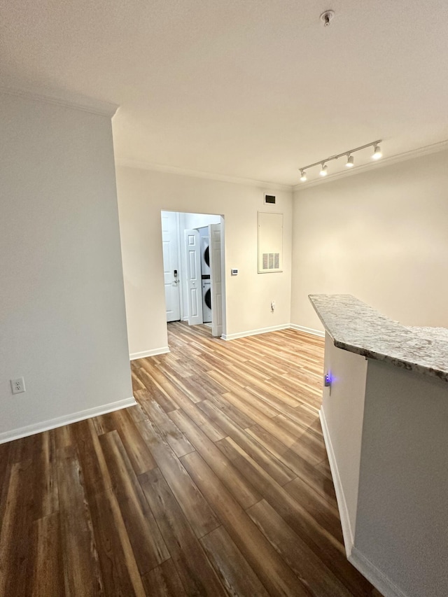 interior space with ornamental molding, track lighting, wood finished floors, stacked washer / dryer, and baseboards