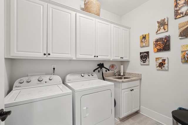 clothes washing area with light wood-type flooring, a sink, washer and dryer, cabinet space, and baseboards