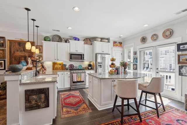 kitchen featuring dark wood-style floors, visible vents, a sink, appliances with stainless steel finishes, and a kitchen breakfast bar