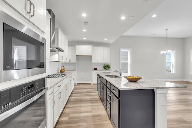 kitchen featuring appliances with stainless steel finishes, sink, white cabinets, hanging light fixtures, and a center island with sink