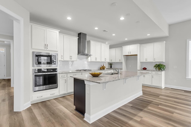 kitchen with stainless steel appliances, white cabinetry, and wall chimney exhaust hood