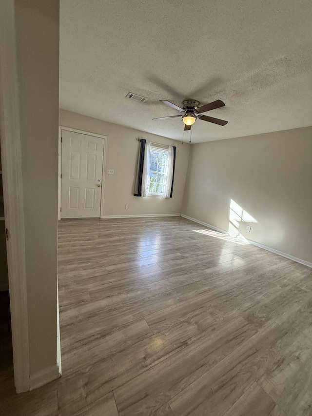 spare room with ceiling fan, a textured ceiling, wood finished floors, visible vents, and baseboards