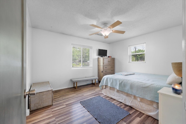bedroom featuring multiple windows, a textured ceiling, wood finished floors, a ceiling fan, and baseboards
