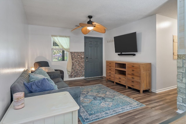 living room with ceiling fan, wood finished floors, baseboards, and a textured ceiling