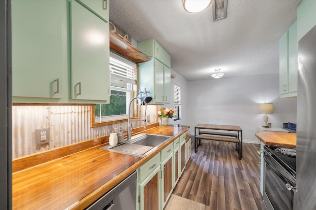 kitchen with green cabinetry, a sink, appliances with stainless steel finishes, wooden counters, and a textured ceiling