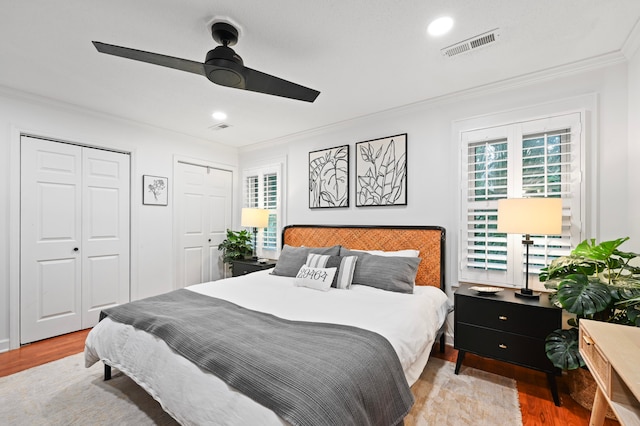 bedroom with ornamental molding, light wood-type flooring, two closets, and ceiling fan