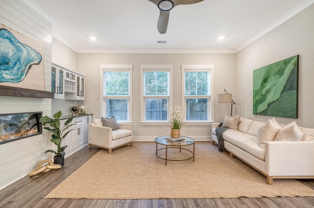 living area with crown molding, visible vents, a large fireplace, wood finished floors, and baseboards